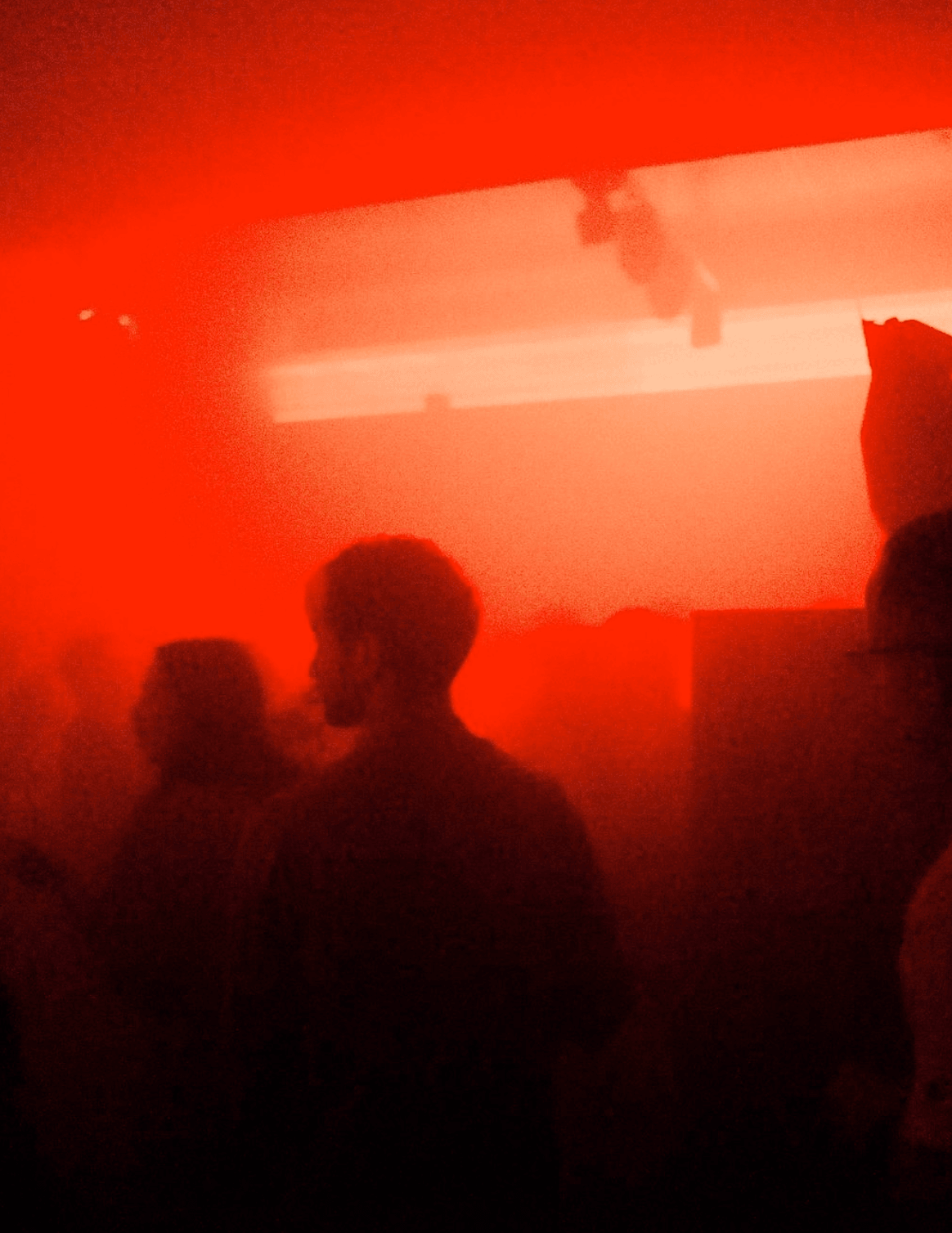 People mingling in a shadowy room, highlighted by bold red lights that add a vibrant touch to the ambiance.